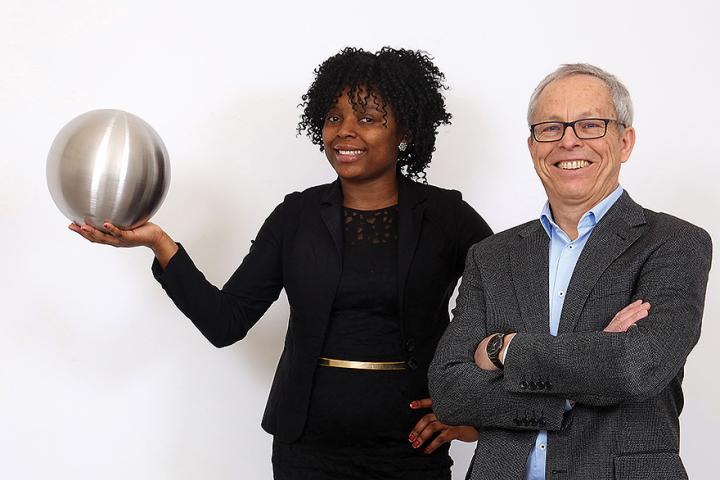 Dr. Gilles Gerbier, holding a silver sphere, and Dr. Alvine Kamaha, with his arms crossed, smile at the camera.