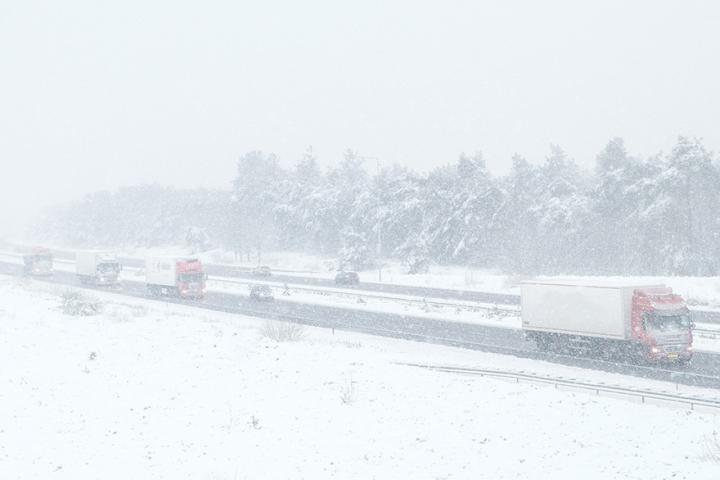 Trucks drive down a highway in a blizzard