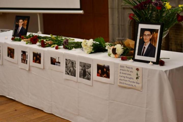 Long table covered in white tablecloth with a photo of Amir Moradi at either end and bouquets of flowers, in between.