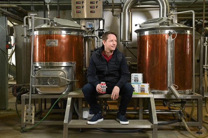 Ted Fleming, Sc’00, sitting on a bench in front of two distillers at his brewery.