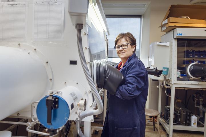 Dr. Crudden standing in the lab wearing a blue lab coat with her arm in a large piece of equipment.
