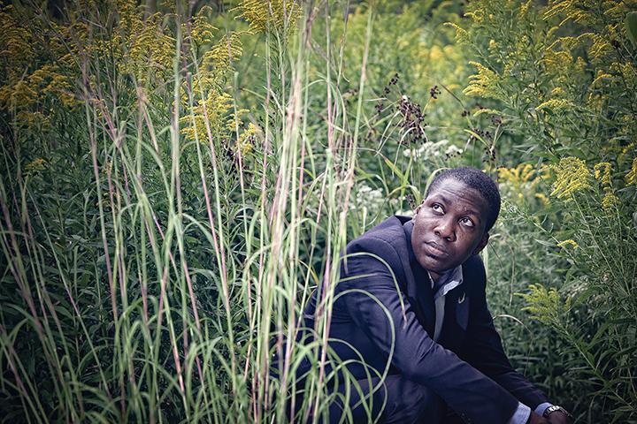 Oluwatobiloba (Tobi) Moody crouching in grass and looking up.