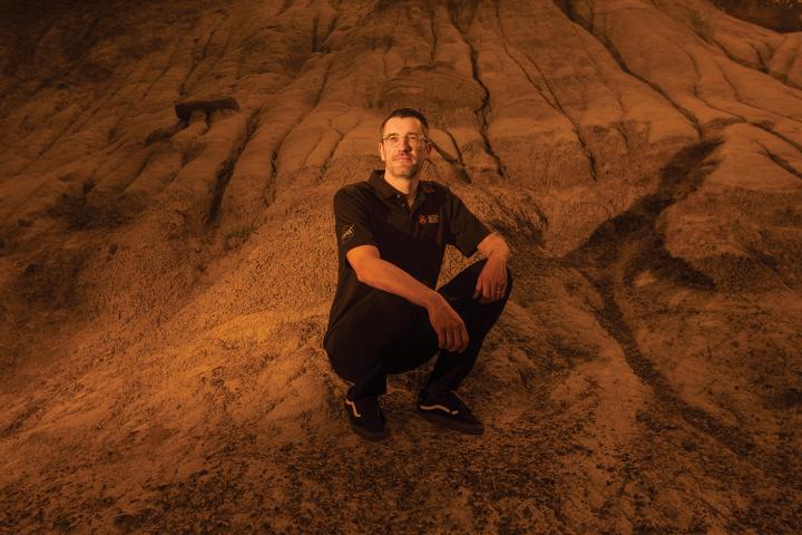 Dr. Chris Herd crouching on a red dirt hill.