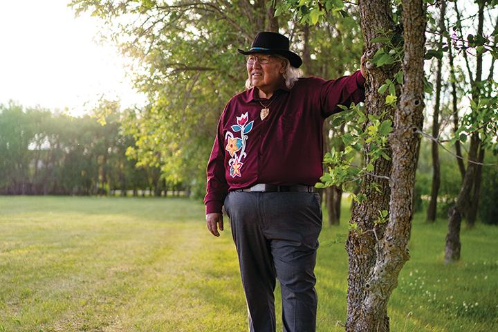 Murray Sinclair standing in the woods with his hand leaning against a tree.