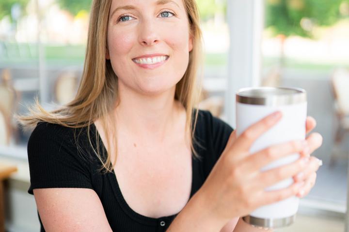 Tara McKenna sitting in a coffee shop, holding a beverage in a reusable mug.