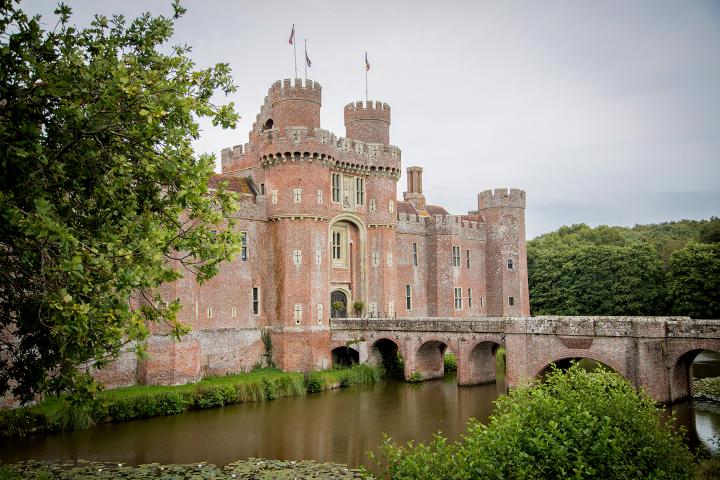 A castle, with a bridge over a moat, and foliage in the foreground.