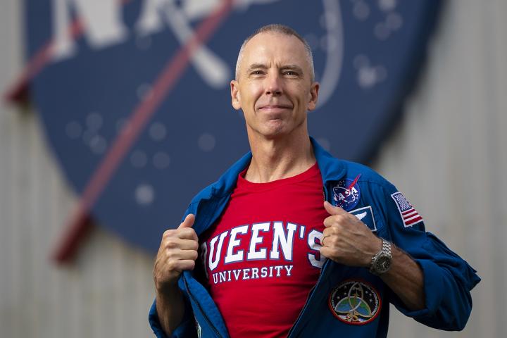 A man holds his zippered down NASA jumpsuit open to reveal a Queen's University T-shirt underneath.