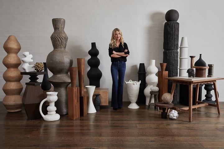 Christiane Lemieux standing with her arms crossed among very tall vases and objects d'art from her product collection.