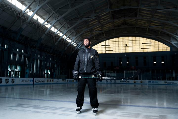 Jaden Lindo on ice in an indoor hockey rink wearing skates, hockey gloves, and holding a hockey stick.