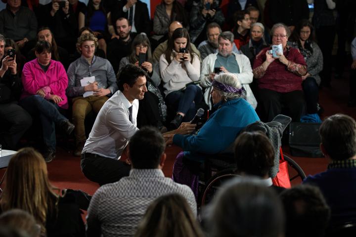 Prime Minister Justin Trudeau kneels on the floor to take a question from Laurel Claus-Johnson, who sits in a wheelchair, during a town hall in Kingston in January 2017.