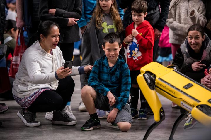 A child kneels down to face a robotic dog.