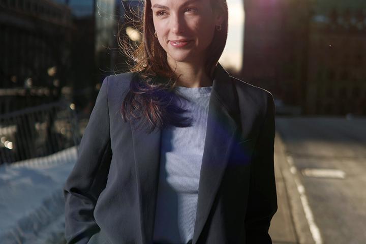 Portrait of a woman in business attire standing outdoors on a city street with sunlight behind her.