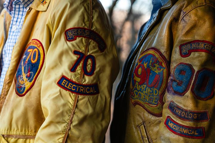 Close-up of two people wearing vintage Queen's jackets with embroidered academic-style patches and insignia.