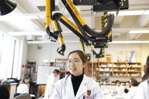 A person smiling in a lab with lots of equipment