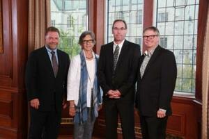 Four people posing for a photo in front of a large window