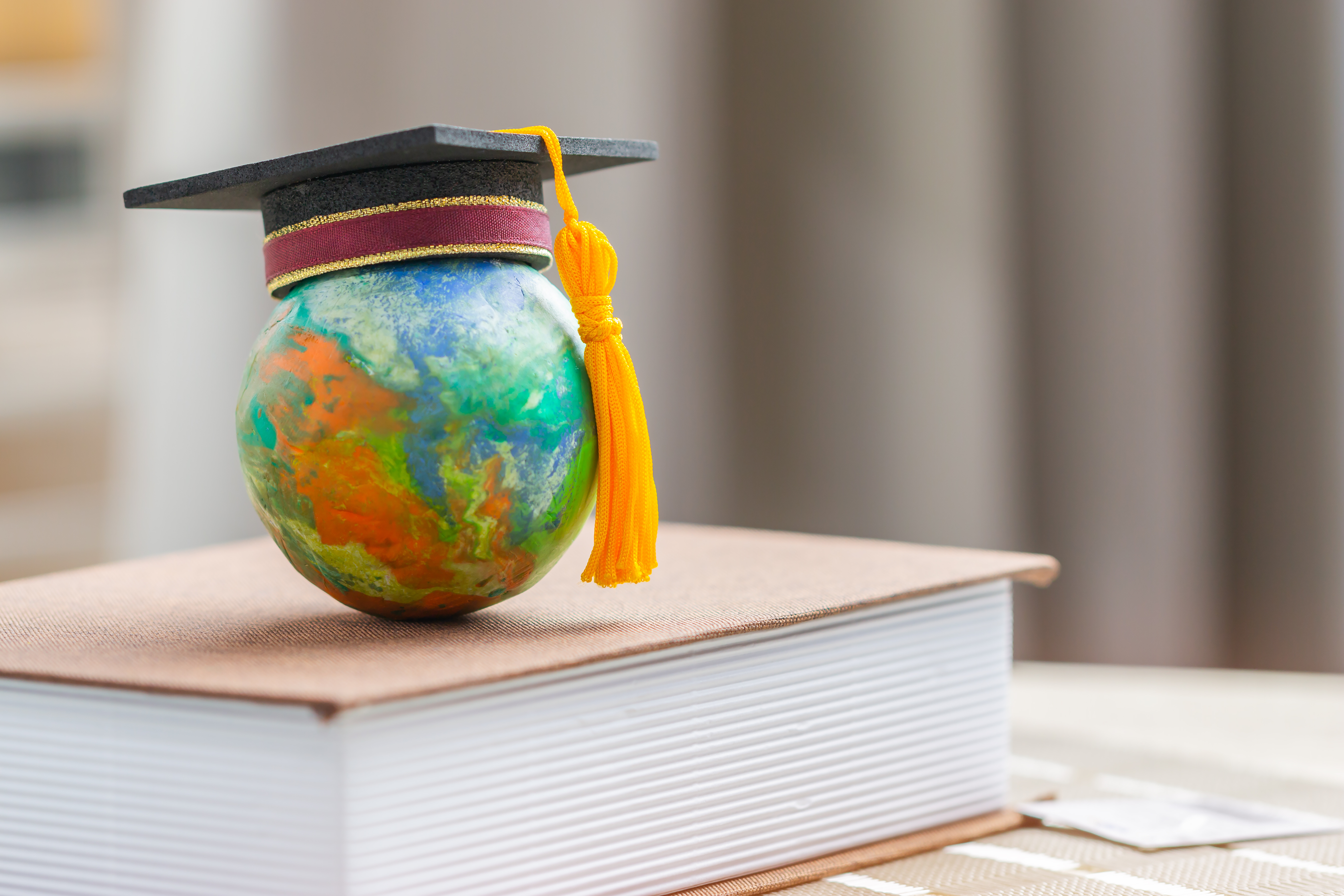 A globe with a graduation hat sits on top of a book.