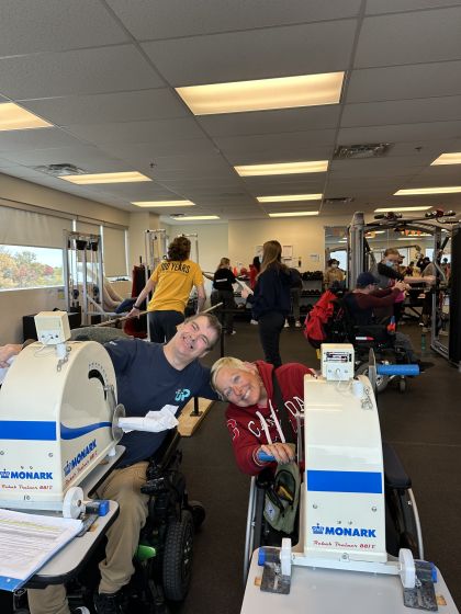 Two students using gym equipment smile for the camera.