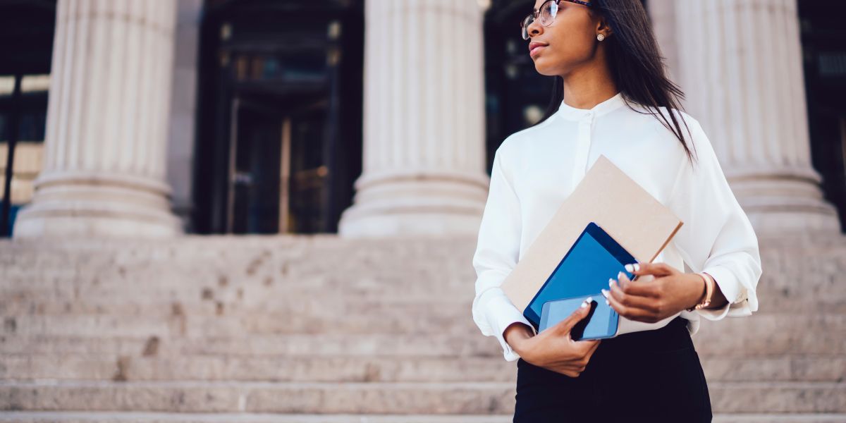 student of faculty of law holding folder and modern gadgets in hands and looking away