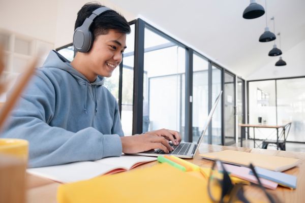Male student sitting at a desk using a laptop and wearing headphones.