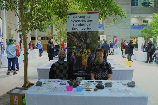 Two people sitting at a table in front of a banner for Geological Studies