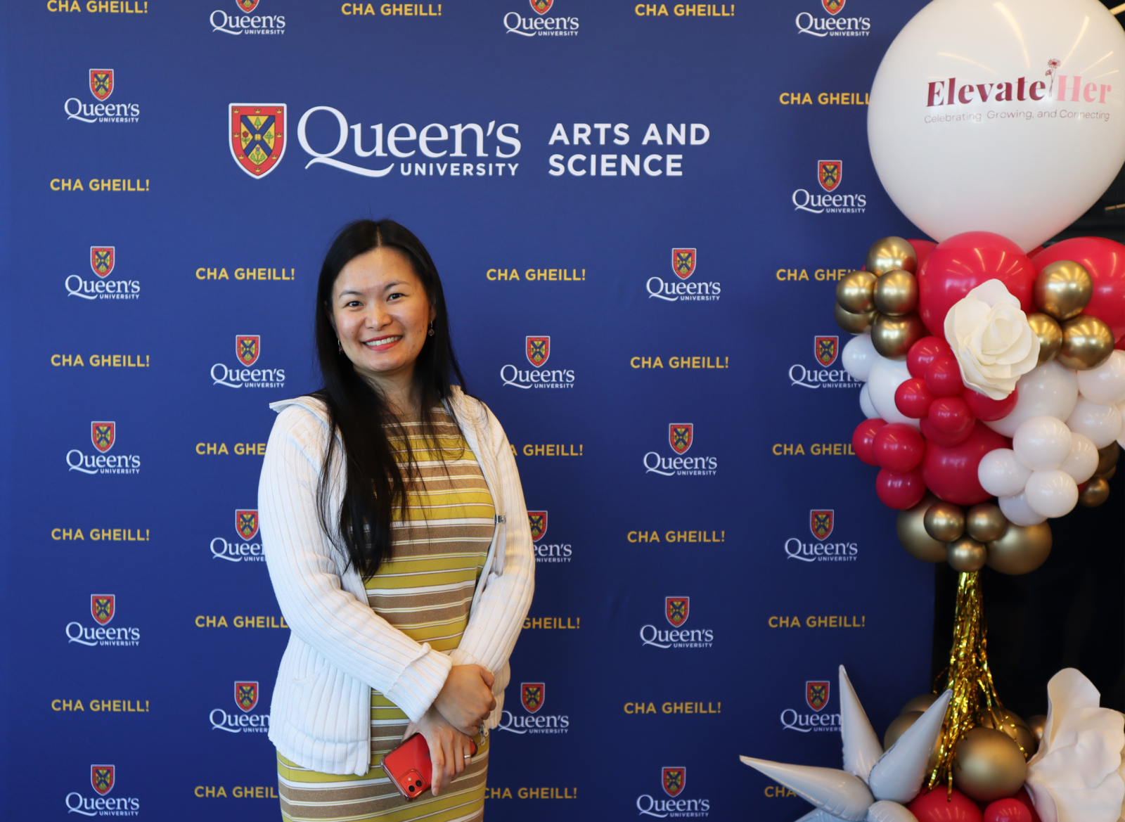 alumna posing in front of Arts and Science blue backdrop at ElevateHer