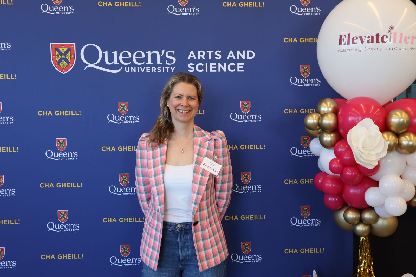 alumna posing in front of Arts and Science blue backdrop at ElevateHer