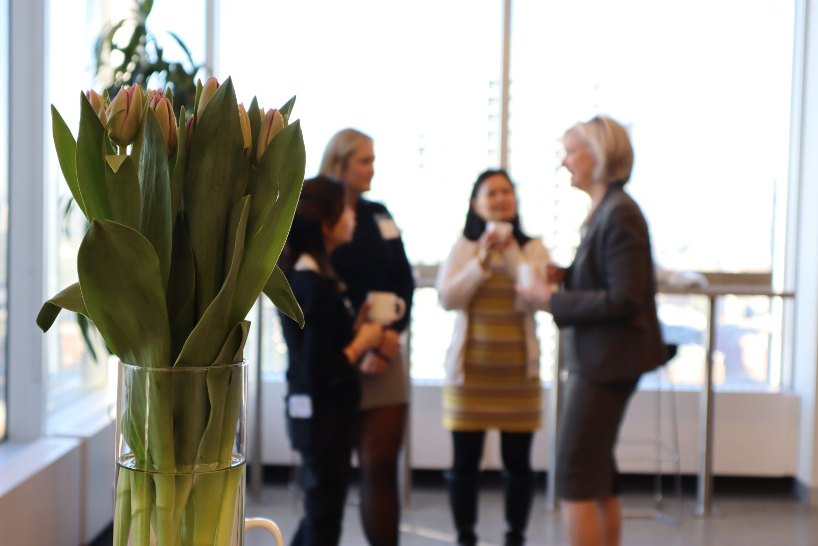Lillies in the foreground with alumni and Dean Barbara Crow speaking in the background at ElevateHer