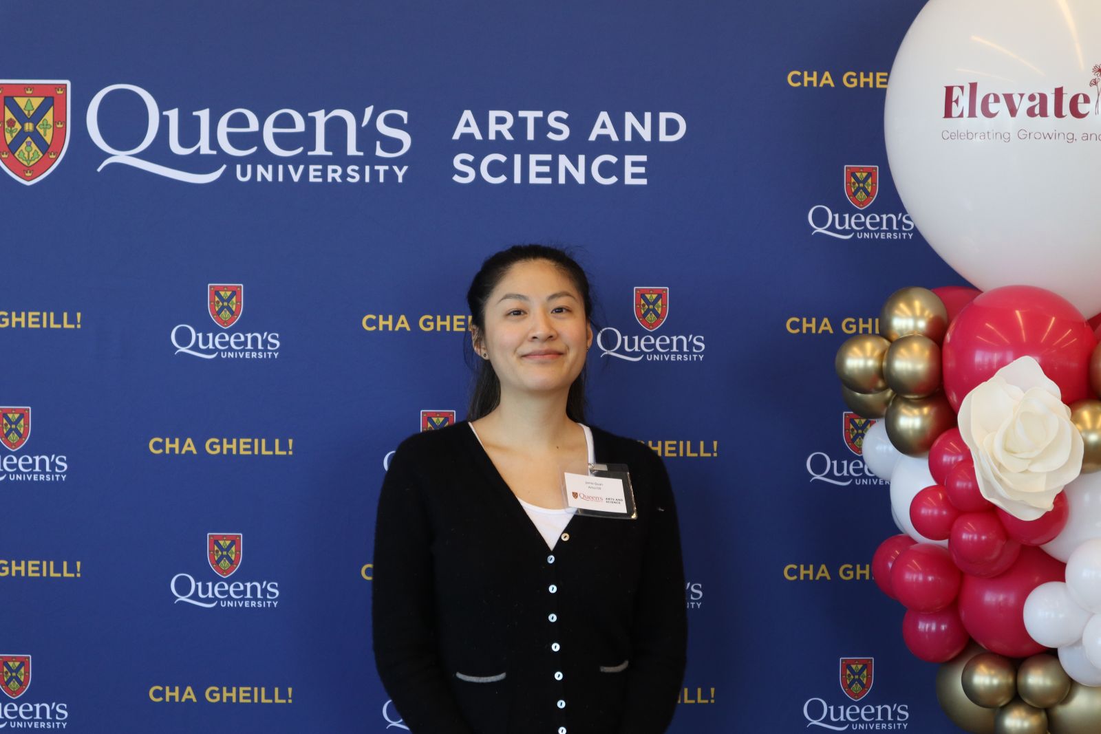 alumna posing in front of Arts and Science blue backdrop at ElevateHer