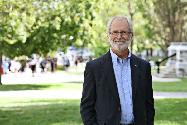 Principal Deane stands on a grassy lawn with trees in the background.
