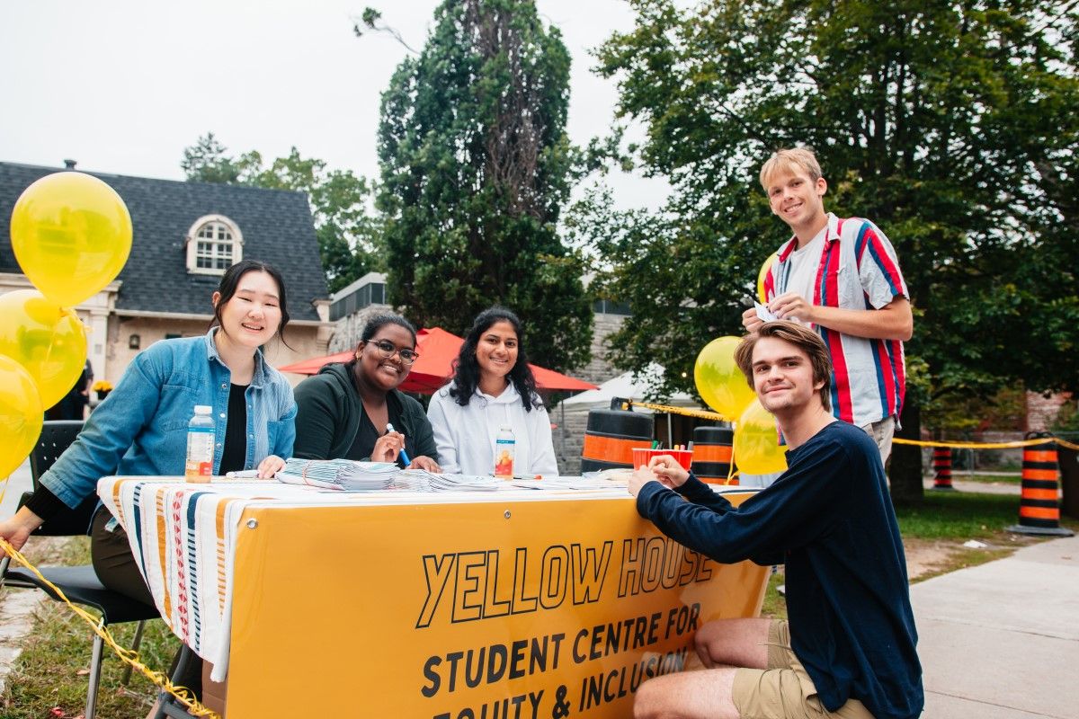 Students standing at a table outside that says Yellow House on it.