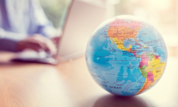 World globe with person typing on laptop in background
