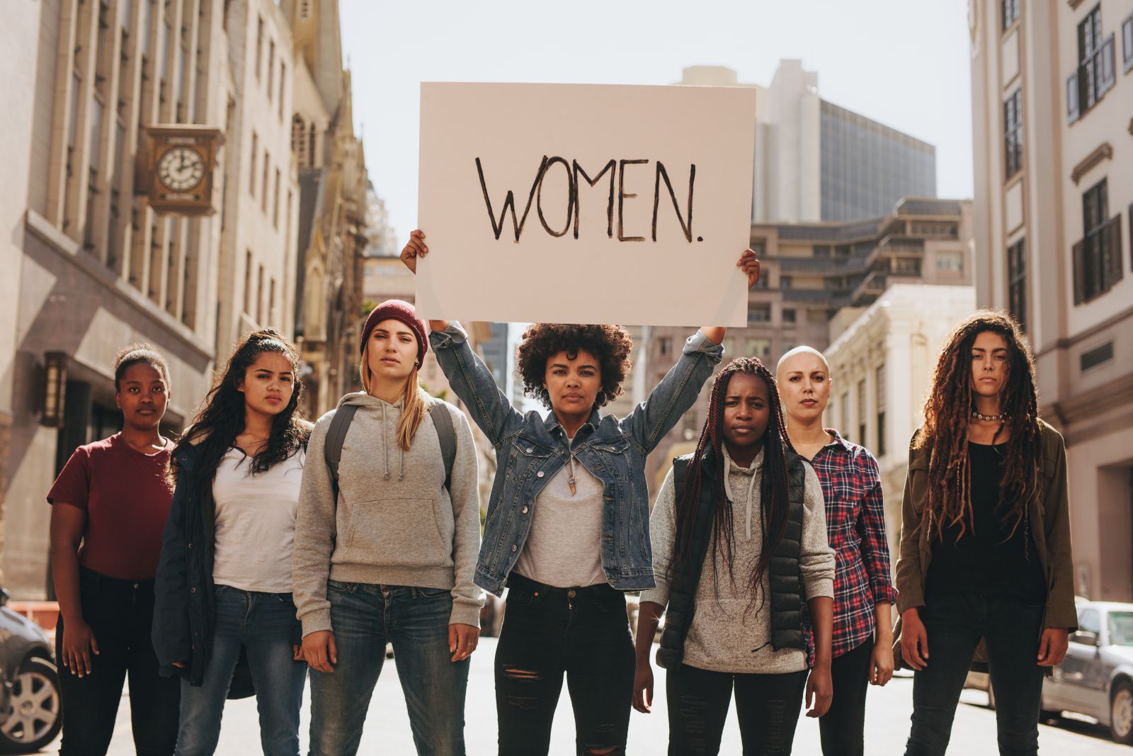 Group of women standing together with the front women holding a sign that says Women