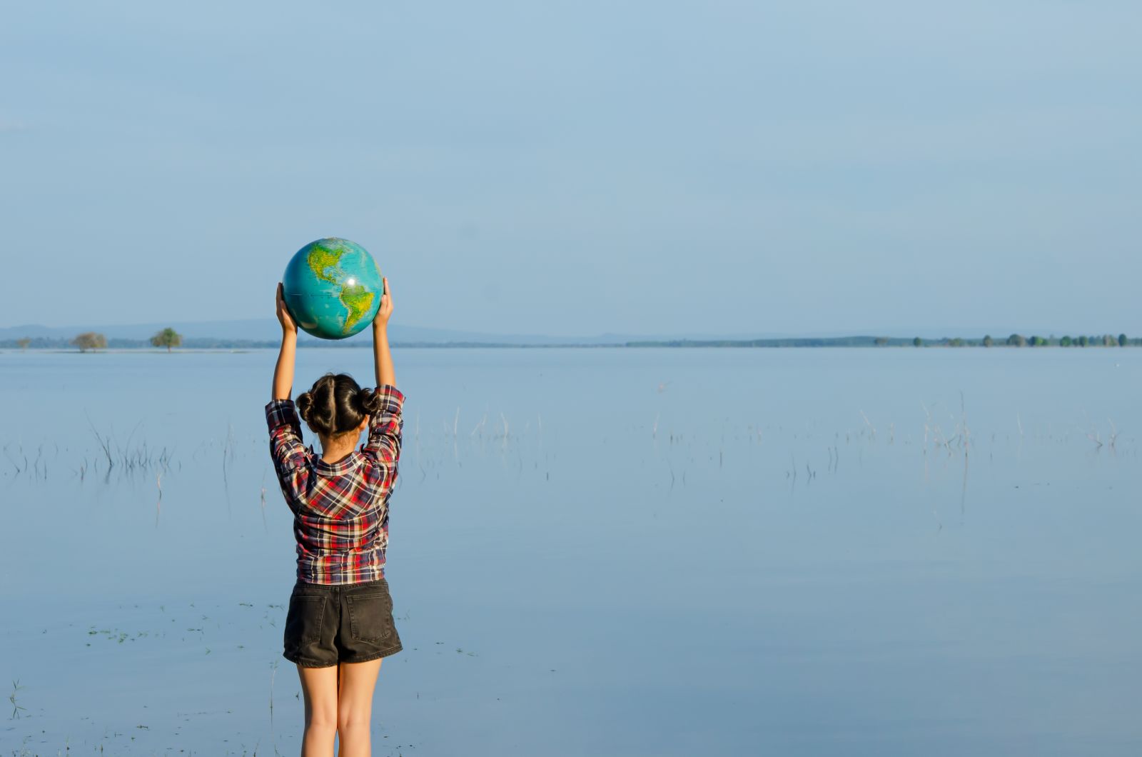 Girl holding a globe above her head, facing the water