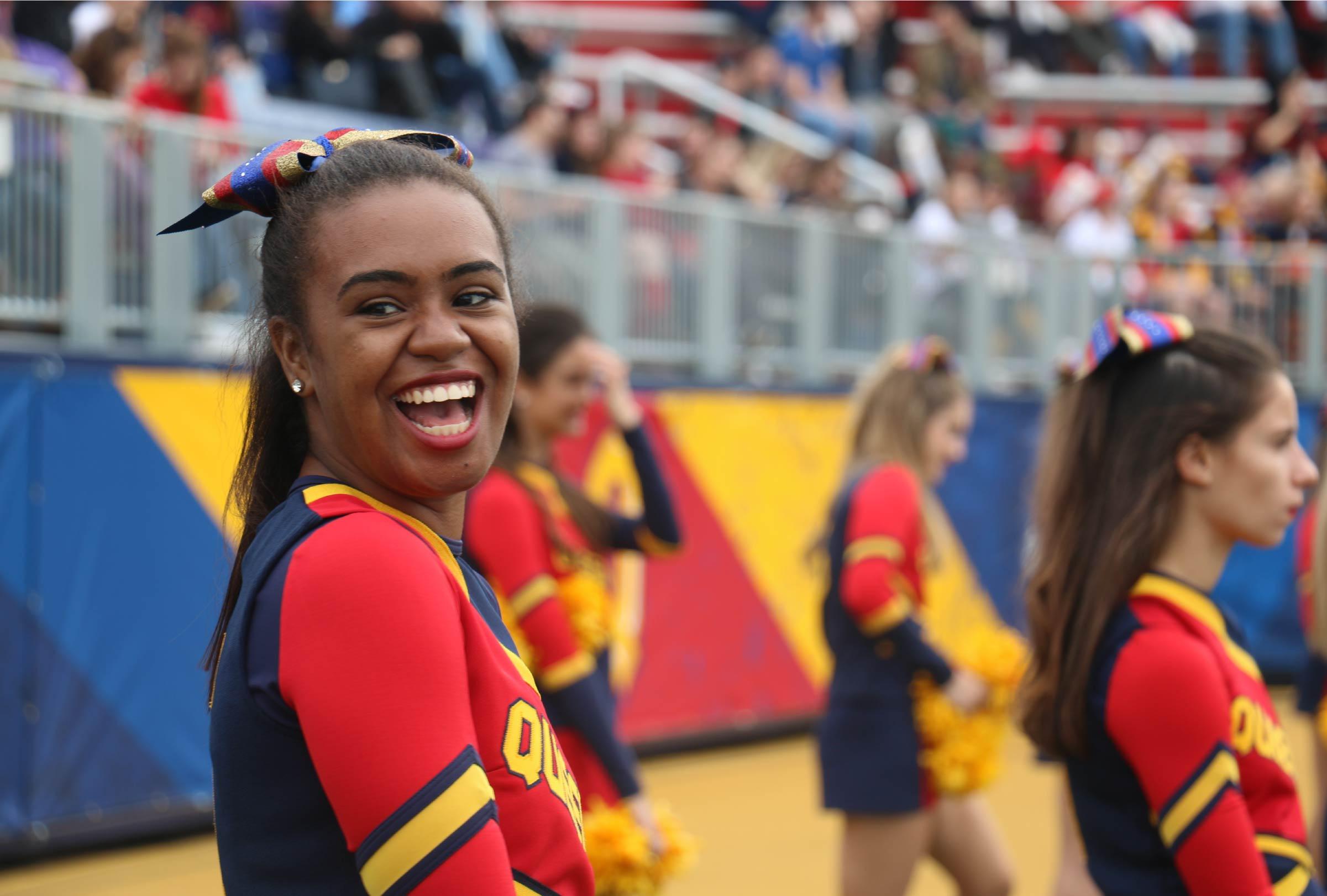 Queen's cheerleader smiling at a football game