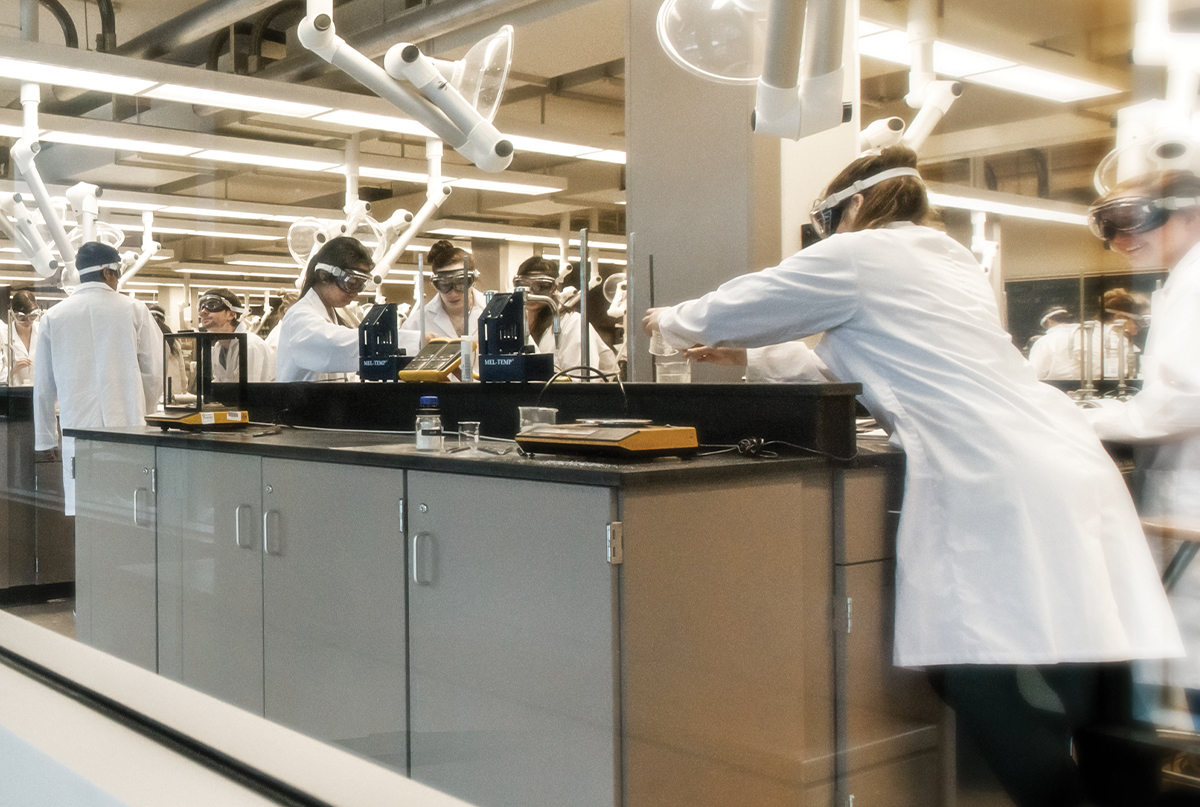 Students wearing lab coats and goggles working in a lab