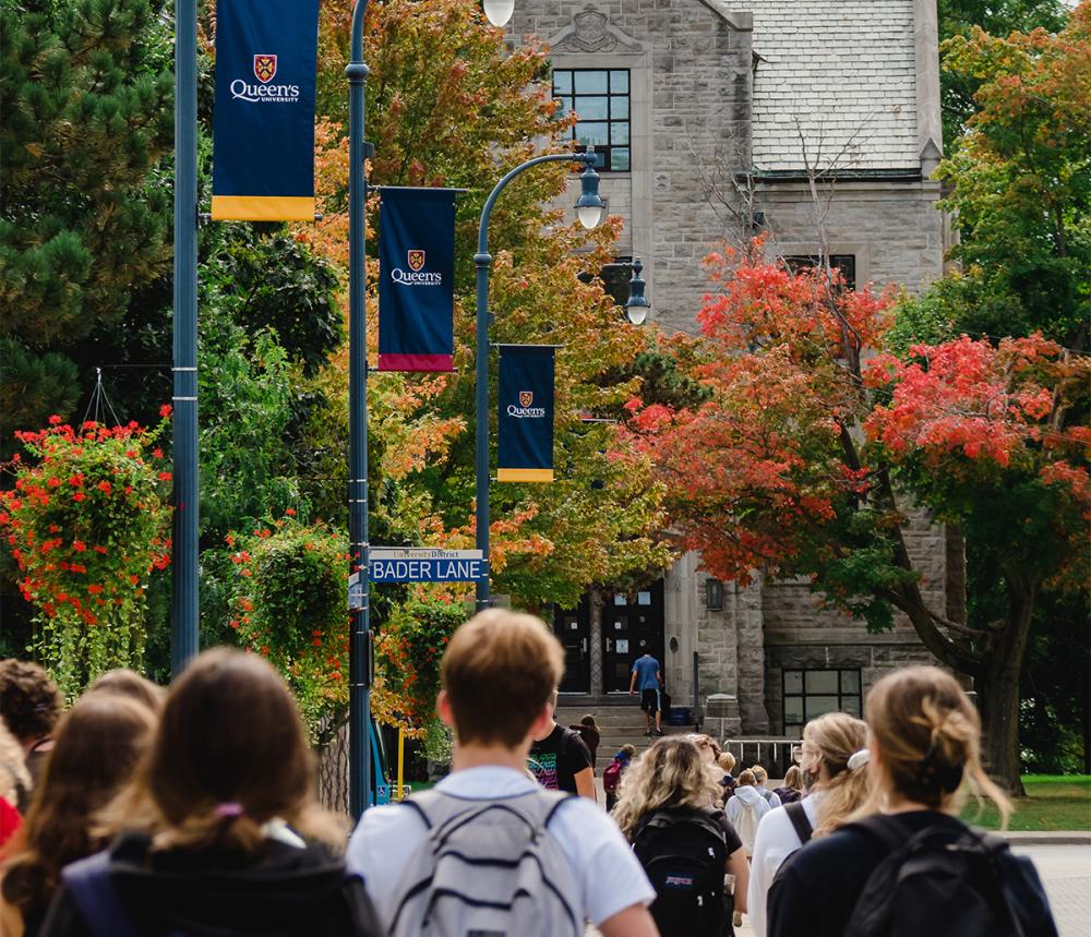 Students walking down University Avenue in the fall, street sign shows Bader Lane. 
