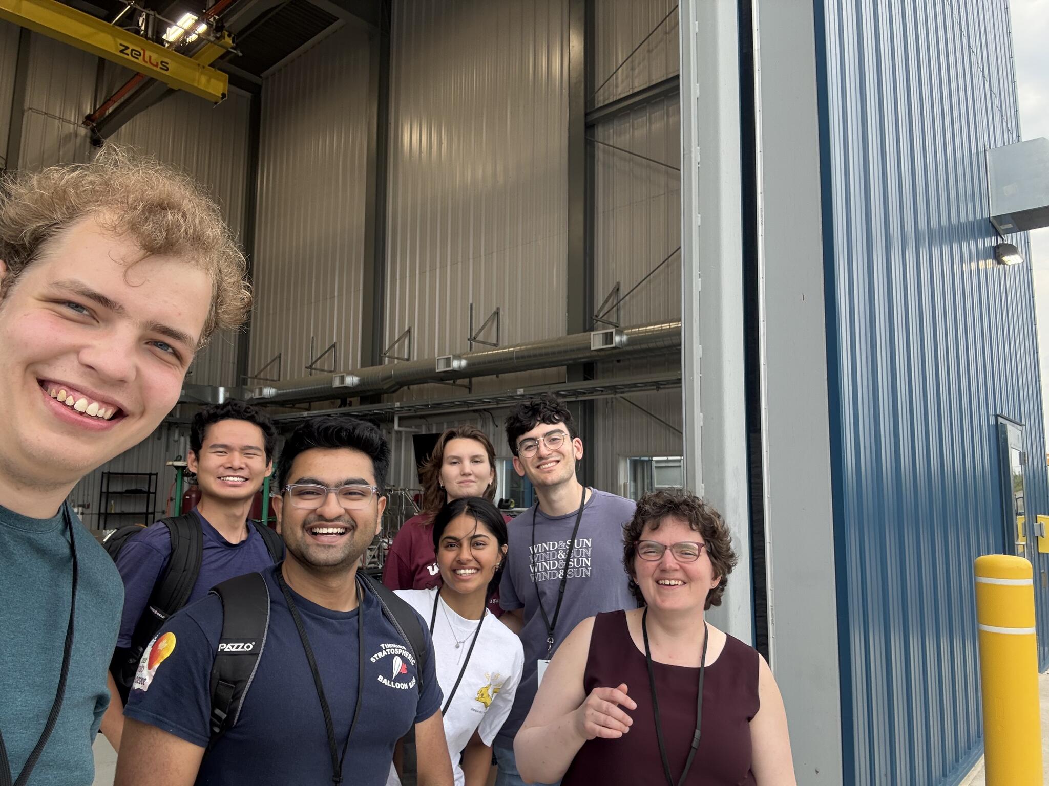 Seven people standing in the open door of a large blue building.