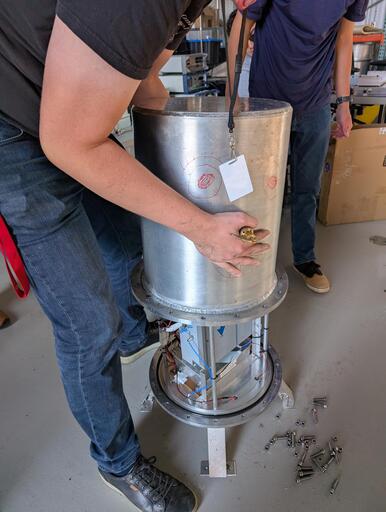 A man removes a metal cover from a vessel containing electronics boxes.