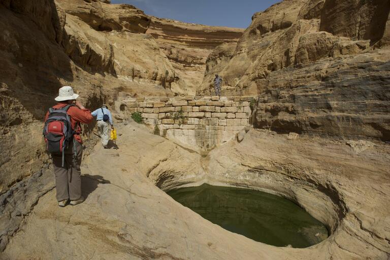 View of a wall with a water collection point in the foreground and rock canyons in the background.