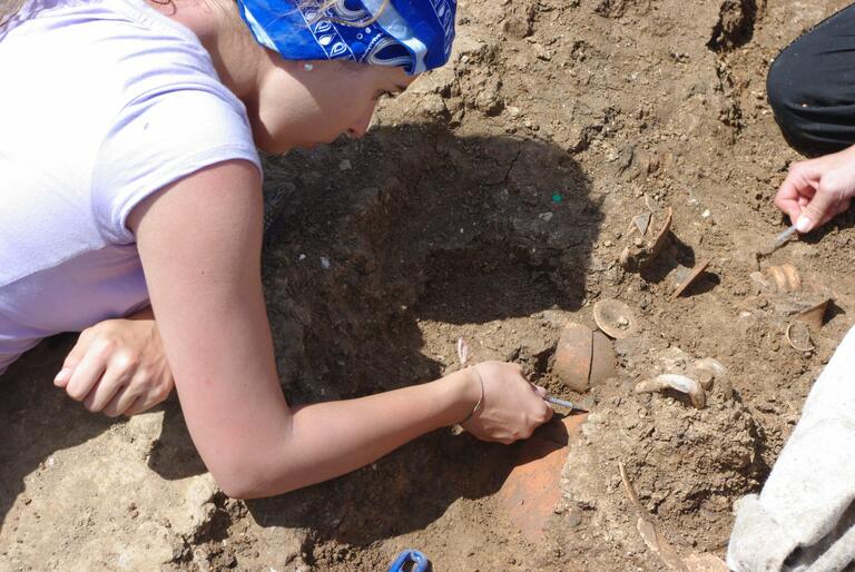 Student carefully uncovering pieces of pottery at Matera dig site.