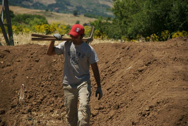 Student carrying pick axes through site at Matera.