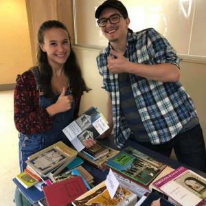 Photograph of two students with a table of books in front of them.