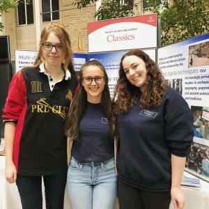 Photograph of three students in front of an information board about Classics as a major.