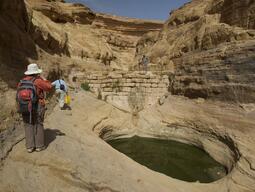 View of a wall with a water collection point in the foreground and rock canyons in the background.