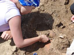 Student carefully uncovering pieces of pottery at Matera dig site.