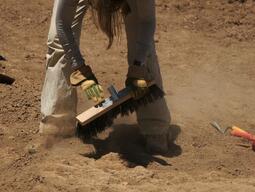 Student using a broom head to carefully sweep away dirt during excavation in Matera.