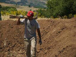 Student carrying pick axes through site at Matera.
