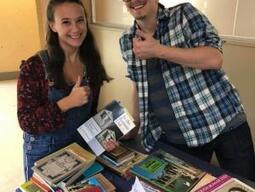 Photograph of two students with a table of books in front of them.