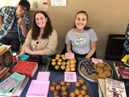 Photograph of three students with a table in front of them bearing books and baked goods.