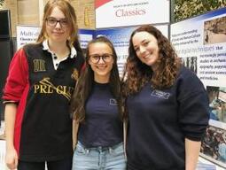 Photograph of three students in front of an information board about Classics as a major.